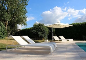 A poolside area with lounge chairs and a large umbrella. - Le Mounet, charmante maison dans le Pays de Serres (Frespech)