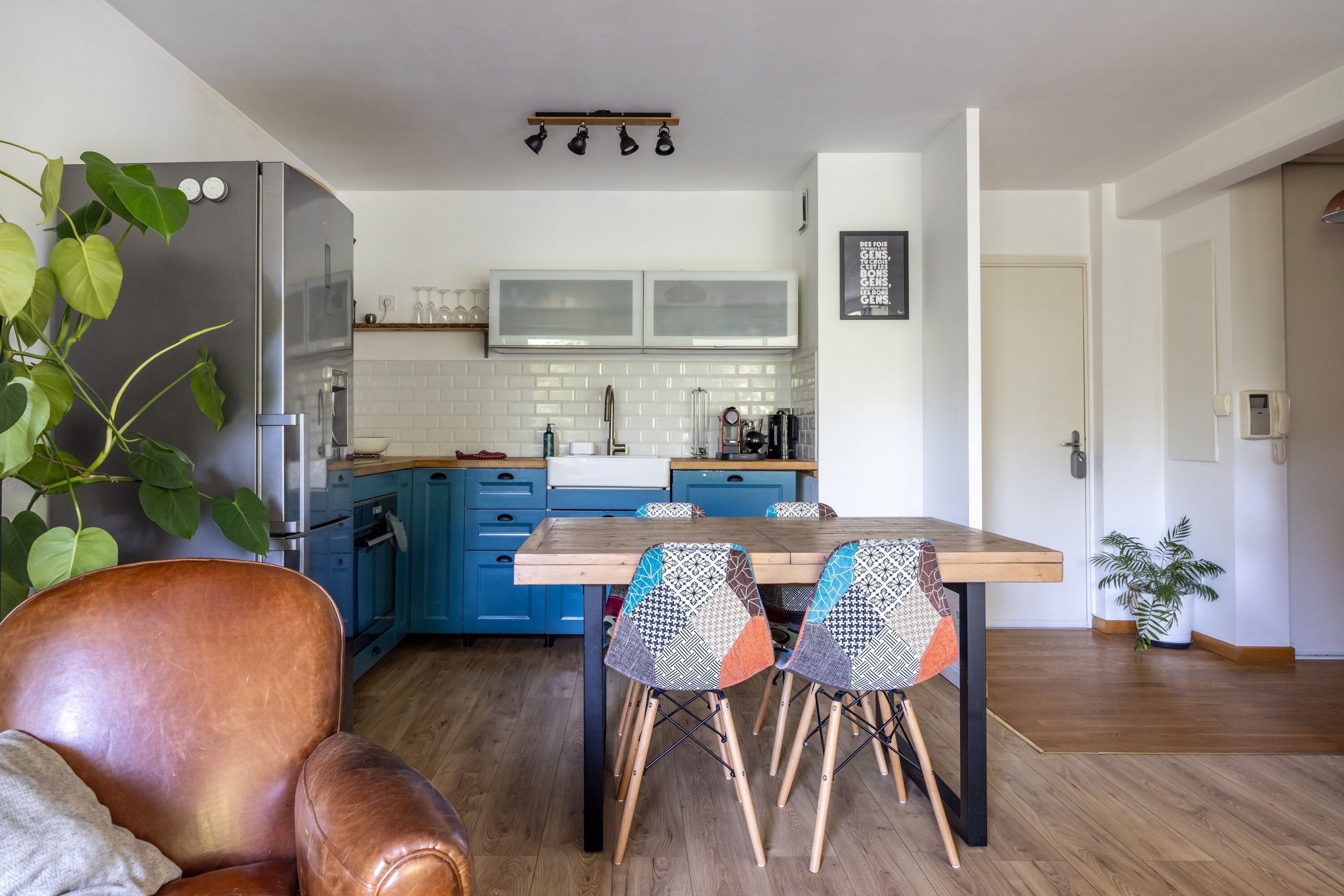 A modern kitchen with a wooden dining table and chairs, a refrigerator, and a blue cabinet.
