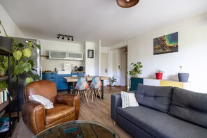 Una sala moderna con un sillón de cuero, un sofá gris, una mesa de centro de vidrio y un comedor con una mesa y sillas de madera.