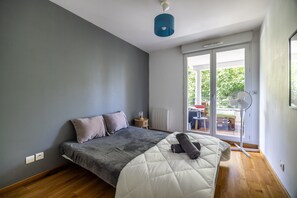 Une chambre à coucher comprenant un lit, une table de chevet, une lampe, un ventilateur et une porte-fenêtre coulissante donnant sur l’extérieur.