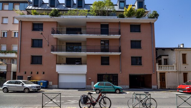 Ein mehrstöckiges Wohngebäude mit Garage, einem Fahrrad und einem geparkten Auto.