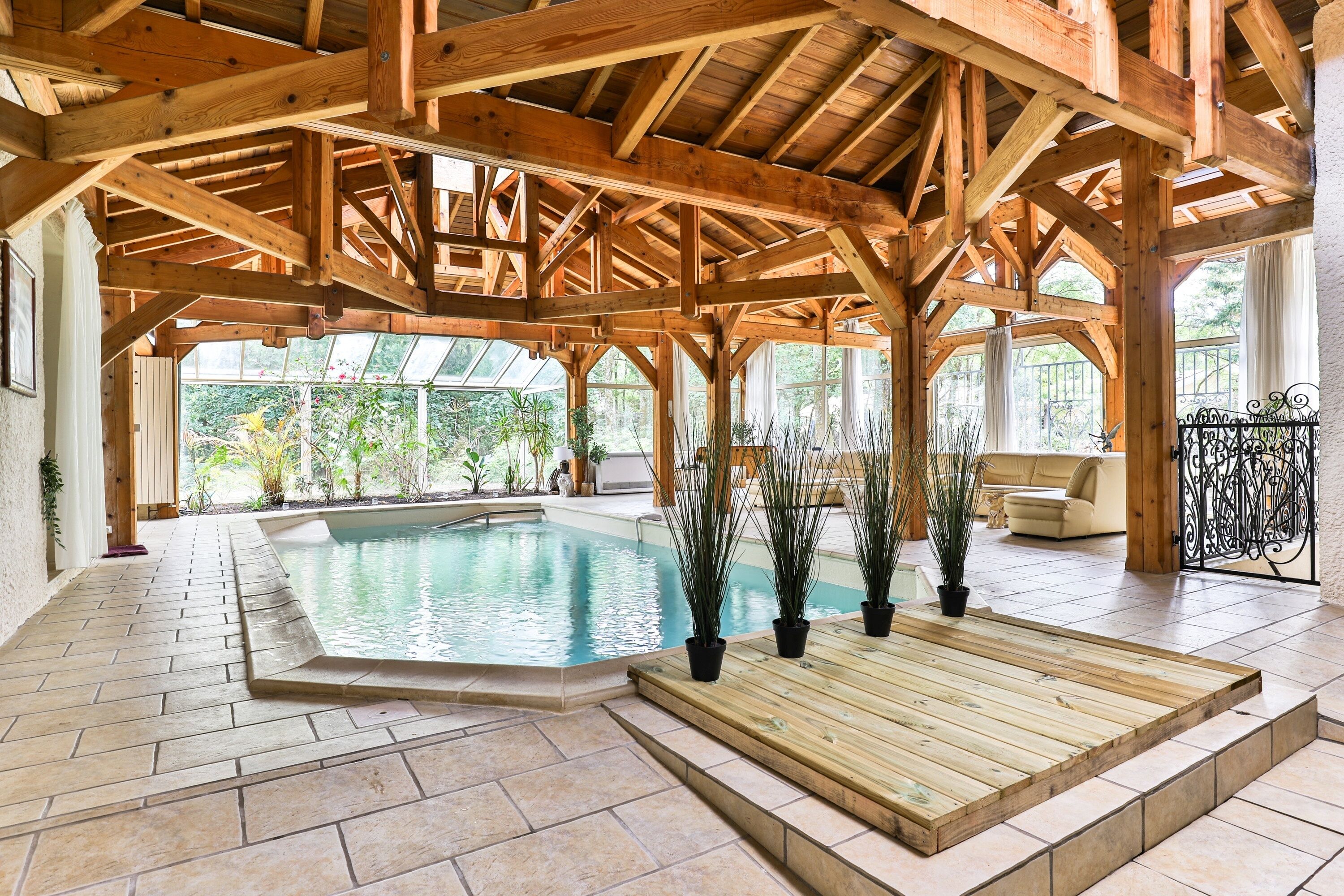 An indoor swimming pool with wooden beams, a tiled floor, and potted plants.