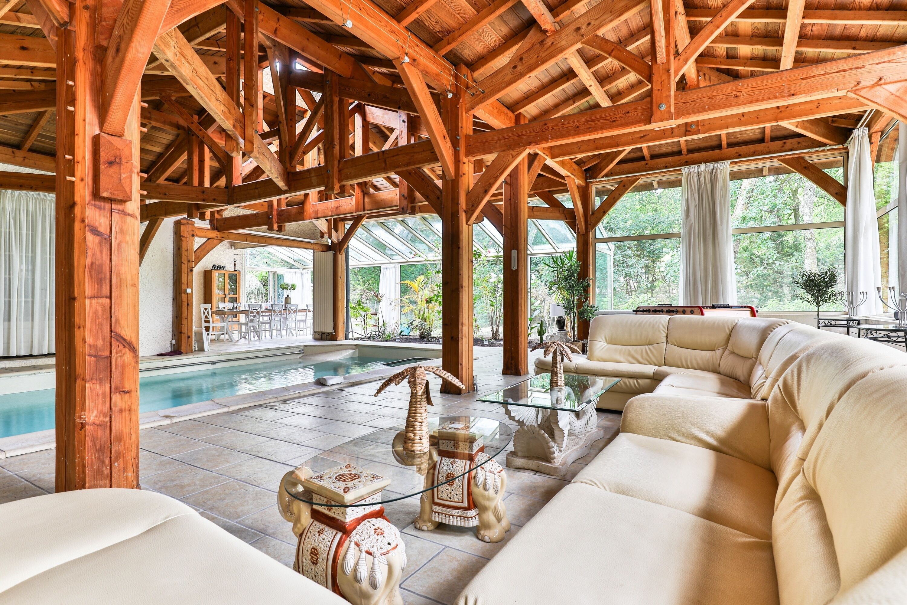 A spacious indoor area with a pool, wooden beams, and a seating area with a glass table.