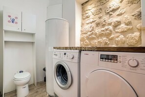 Une salle de bain moderne équipée d’un lave-linge, de toilettes et d’un mur décoratif en pierre.