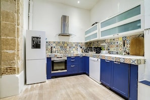 Cozinha com armários azuis, geladeira branca, painel de azulejos e exaustor em aço inoxidável.