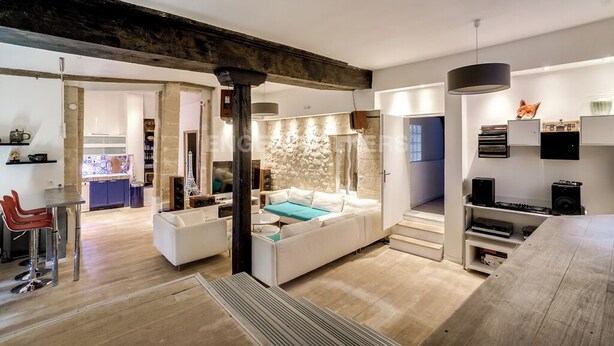 A modern living room with a sofa, a dining area with chairs, a kitchen in the background, and a staircase leading to another level. - LUXURY LOFT IN THE HEART OF PARIS (Paris)