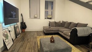 Un salon comprenant un canapé d’angle, un téléviseur à écran plat, une guitare et une petite table sur laquelle est posé un globe terrestre.