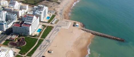 Vista aérea de una zona costera con playa, un muelle y edificios residenciales.