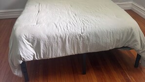 Un letto in una stanza con pavimento in legno e una finestra con persiane.