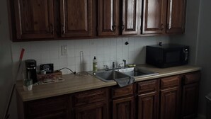 Una cucina con mobili in legno, un forno a microonde, un lavello e un piano di lavoro con diversi oggetti.