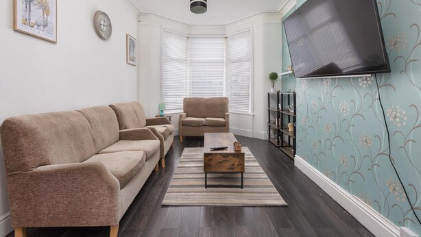 Ein Wohnzimmer mit Sofa, Sesseln, Couchtisch, Fernseher und einer Wand mit Muster.