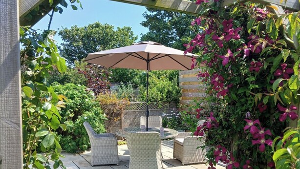 Eine Terrasse im Freien mit Korbmöbeln, einer Pergola und blühenden Pflanzen.