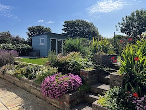 Ein kleines blaues Haus, umgeben von einem Garten mit verschiedenen Pflanzen und Blumen.