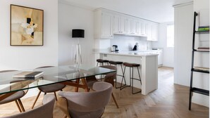 Una cocina moderna con armarios blancos, una isla central con taburetes y una mesa de comedor de vidrio con sillas.