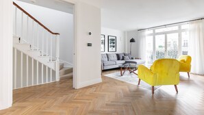 Una sala de estar moderna con piso de espiga, una escalera, un sofá gris y sillones amarillos.