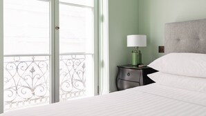 A hotel room with a bed, a nightstand with a lamp, and a view through a window with a decorative iron railing. - Spring Gardens - One Bedroom Apartment, Sleeps 2 (London)