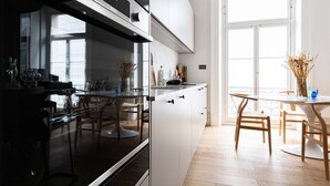 A modern kitchen with white cabinetry, a black oven, and a dining area with a round table and chairs. - Spring Gardens - One Bedroom Apartment, Sleeps 2 (London)