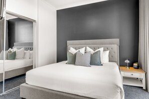 A modern bedroom with a grey upholstered headboard, a white bedspread, and a bedside table with a lamp. - Chevron Renaissance River View (Surfers Paradise)