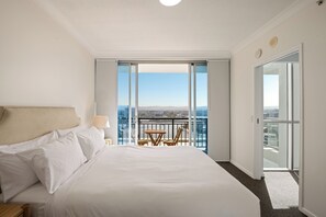 Habitación de hotel con una cama grande, una mesita pequeña y un balcón con vista a la ciudad.