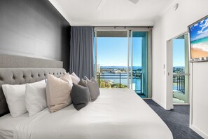Ein modernes Hotelzimmer mit einem großen Bett, Blick auf Stadt und Wasser sowie einem Balkon mit Glastür.
