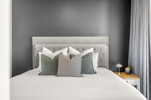 A bed with a grey upholstered headboard, white bedding, and patterned pillows. - Chevron Renaissance River View (Surfers Paradise)