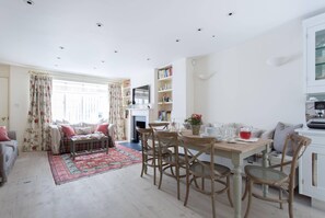 Ein Wohnzimmer mit einer Couch, einem Esstisch mit Stühlen, einem Kamin und einem Bücherregal.