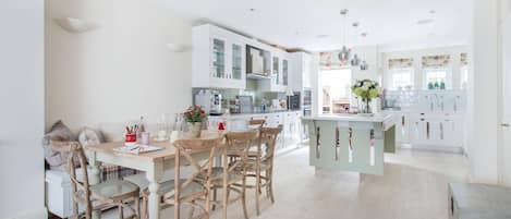 A modern kitchen with white cabinets, a wooden dining table, and a central island.