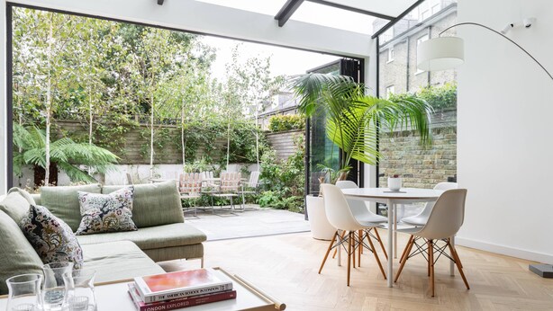 A modern living room with a glass wall, a dining area, and a garden view. - South End Green II - Five Bedroom House, Sleeps 10 (Hampstead)