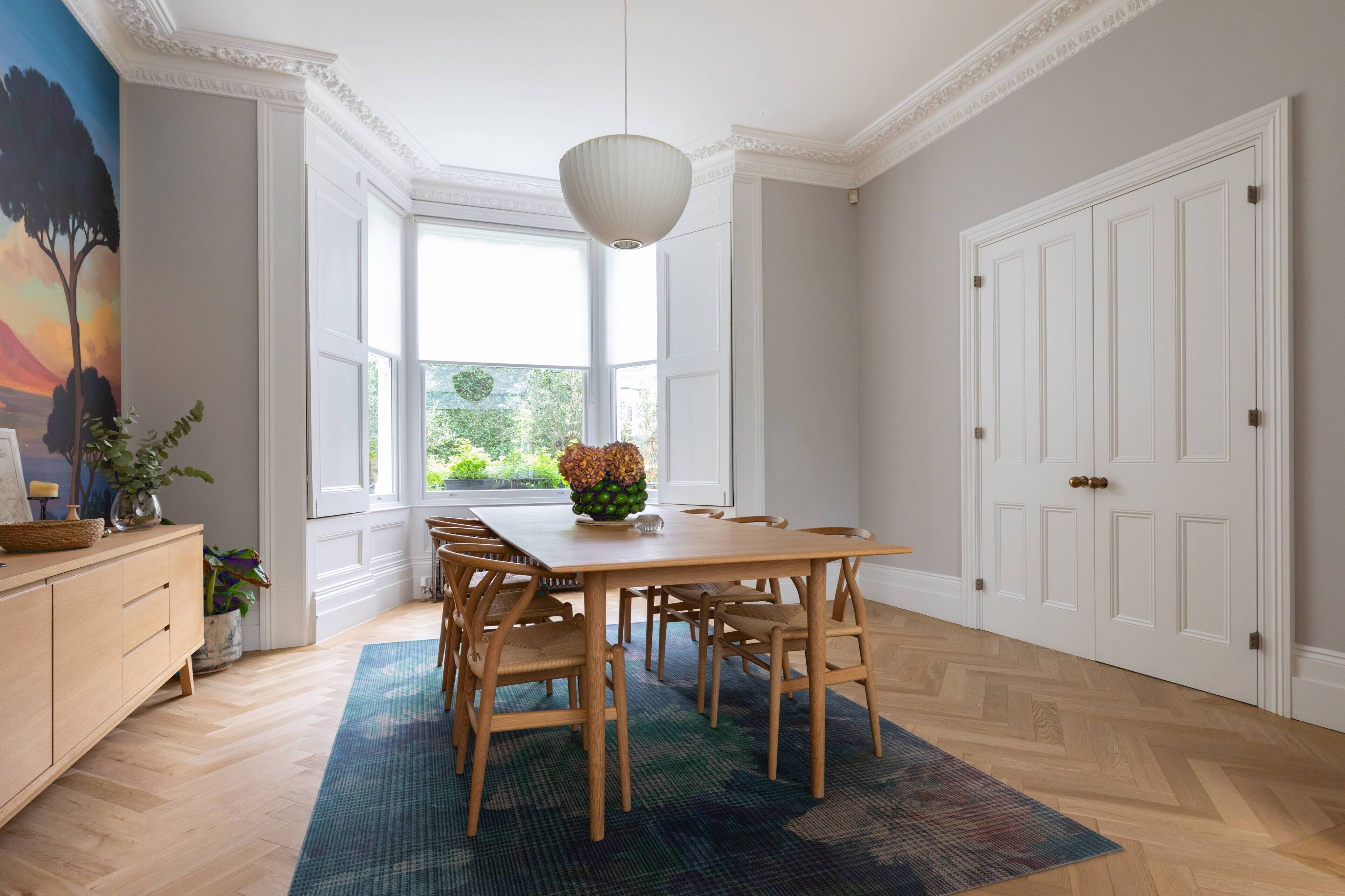 A dining room with a wooden table, chairs, a rug, a hanging light fixture, and a door with a white frame.
