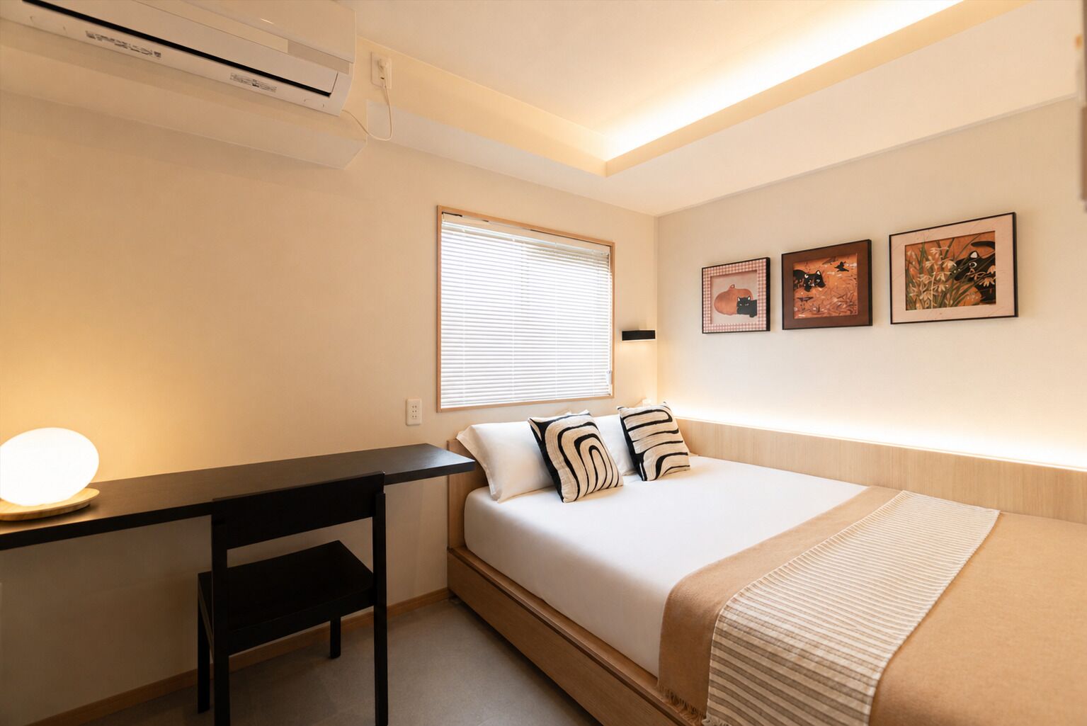 A bedroom with a bed, bedside table, lamp, air conditioning unit, window with blinds, and wall-mounted artwork.