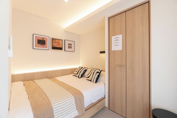 A bedroom with a bed, a wooden wardrobe, and three framed pictures on the wall.