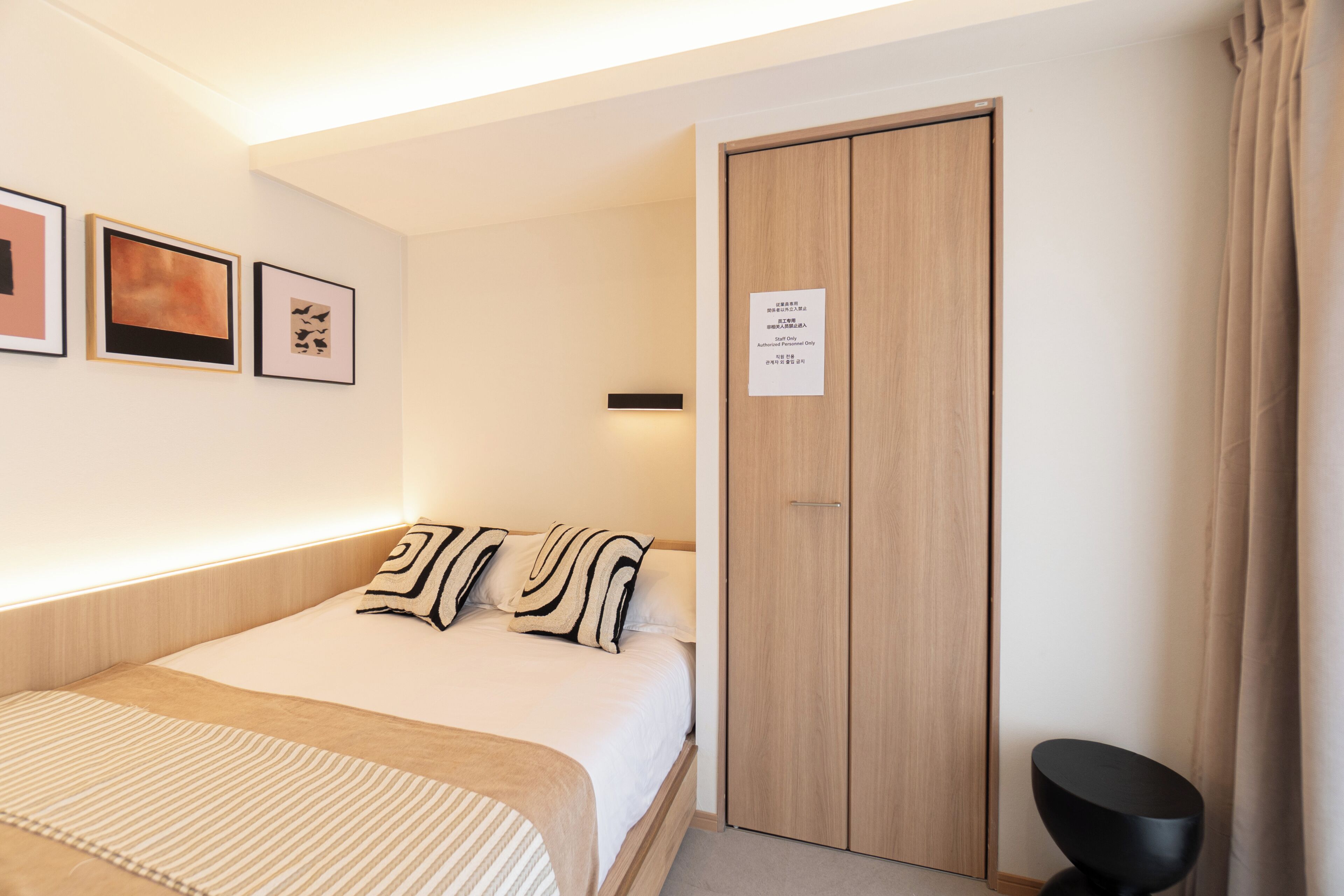 Habitación de hotel con una cama, un armario y un taburete negro pequeño.