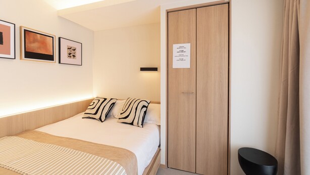 Een hotelkamer met een bed, een kledingkast en een klein zwart krukje.