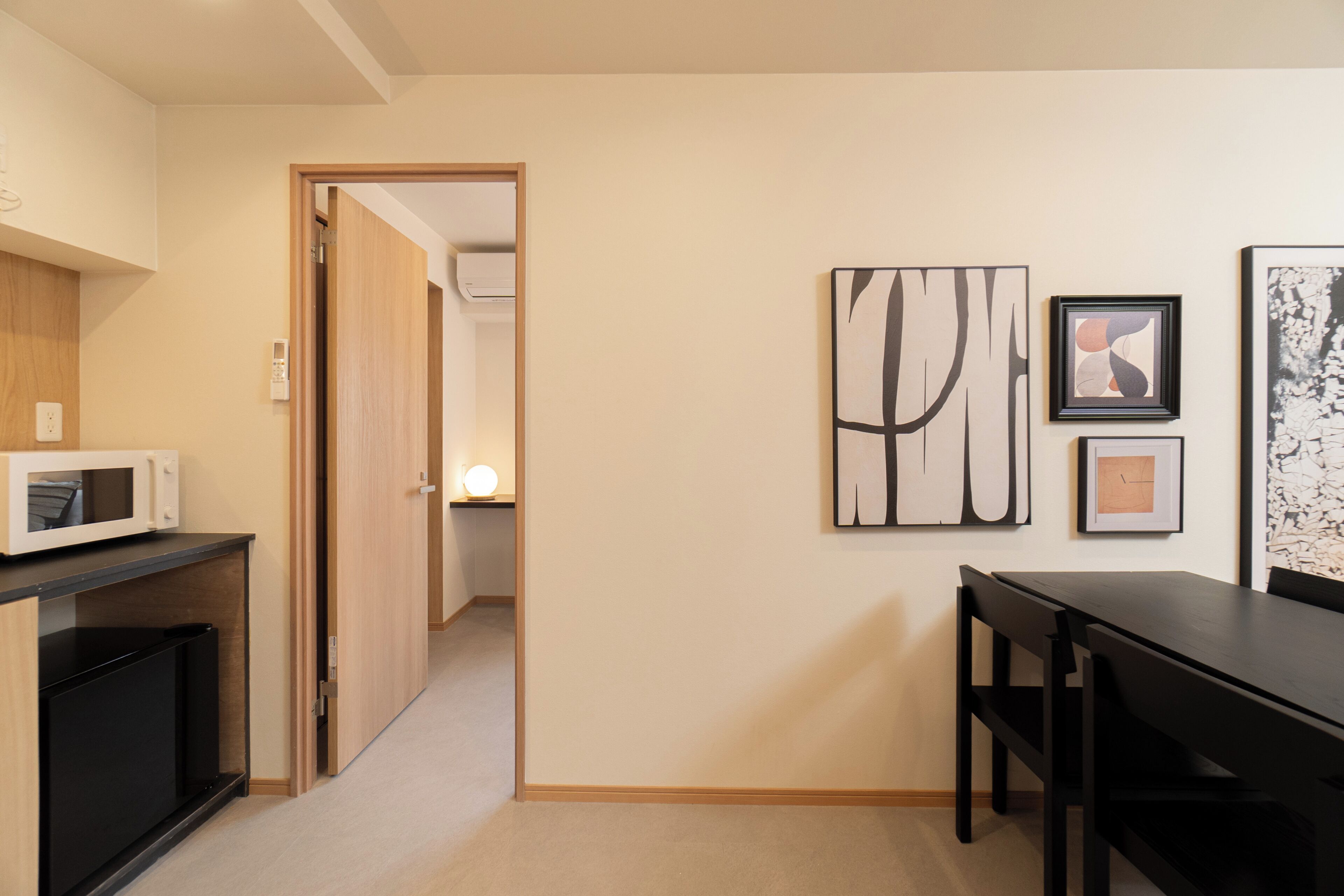 A hallway with a microwave, a table, chairs, and artwork on the wall.