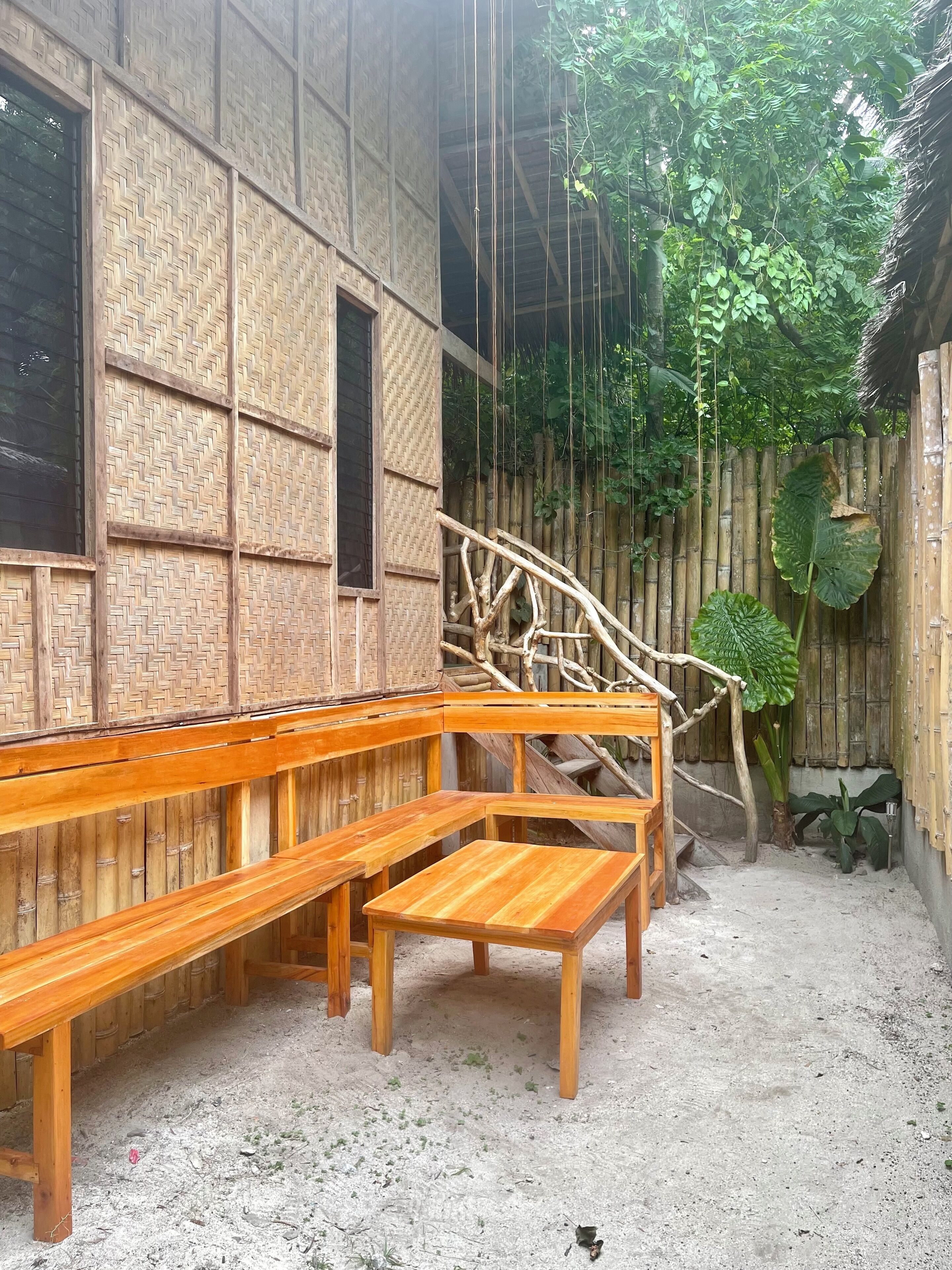 Un área con bancos de madera, pared de bambú y estructura de techo de paja.