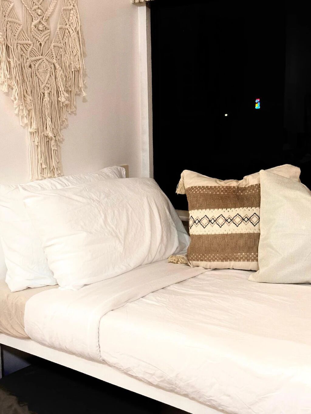 A bed with white bedding and a macramé wall hanging.