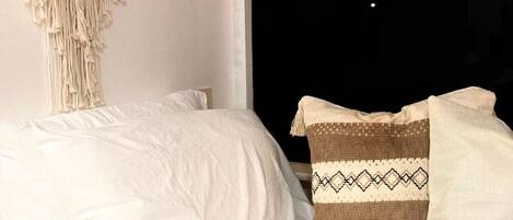 A bed with white bedding and a macramé wall hanging.