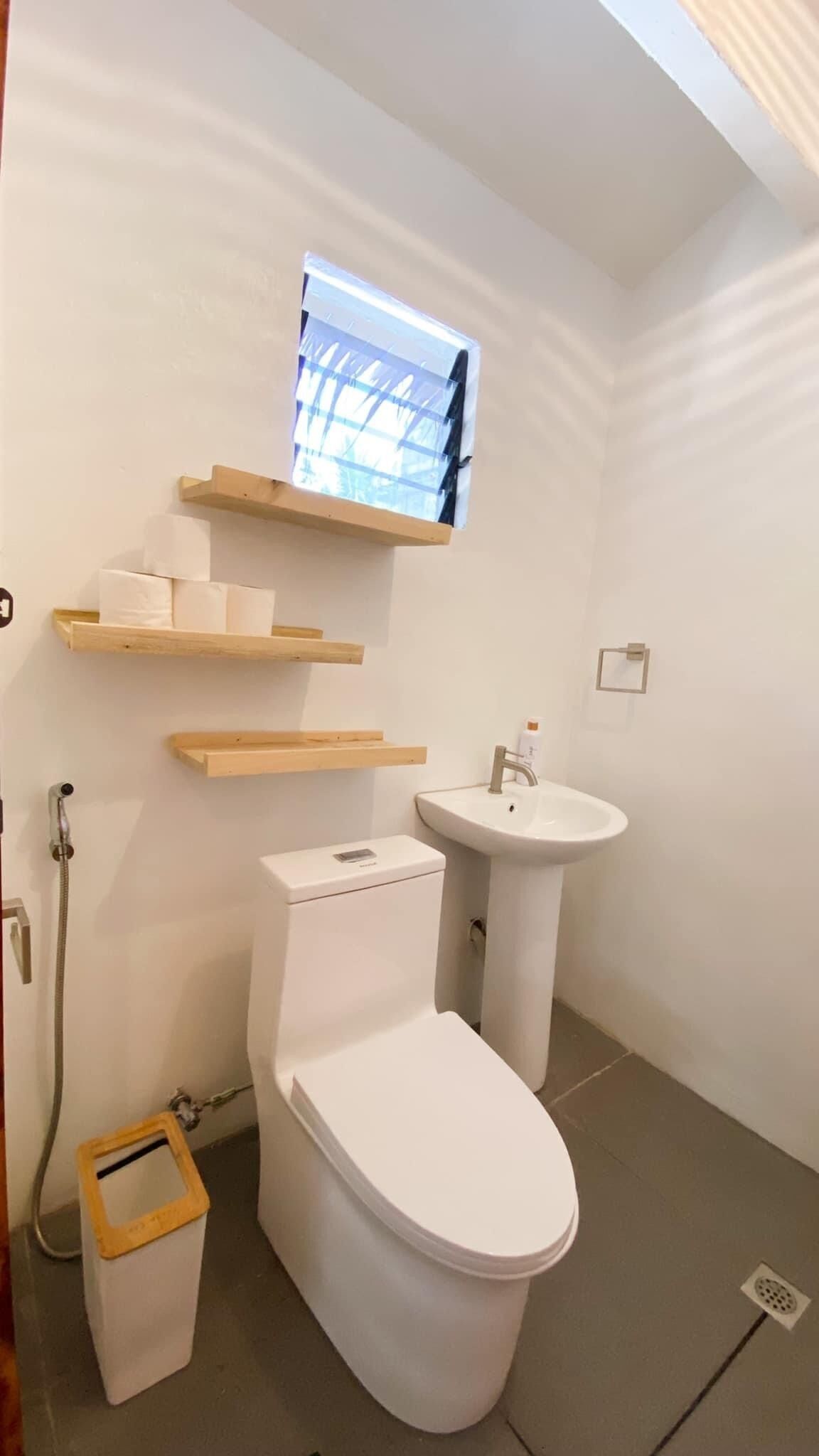 A small, modern bathroom with a toilet, sink, and wooden shelves.