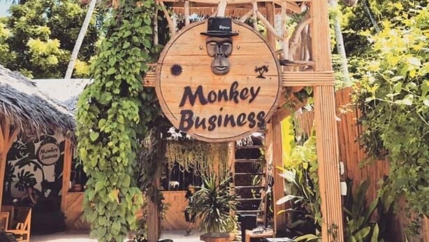 Una estructura de madera con un letrero que dice 'Monkey Business', rodeada de abundante follaje y plantas.