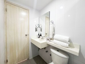 Un baño con inodoro, lavamanos, espejo y toallero.