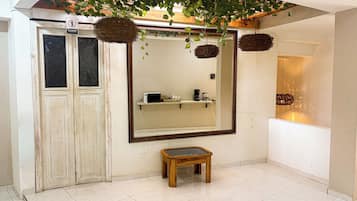 A bathroom with a large mirror, a small wooden stool, and a shelf with toiletries.