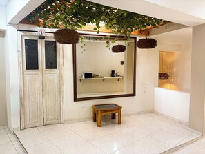 Un baño con un espejo grande, un taburete de madera y un estante con artículos de aseo.