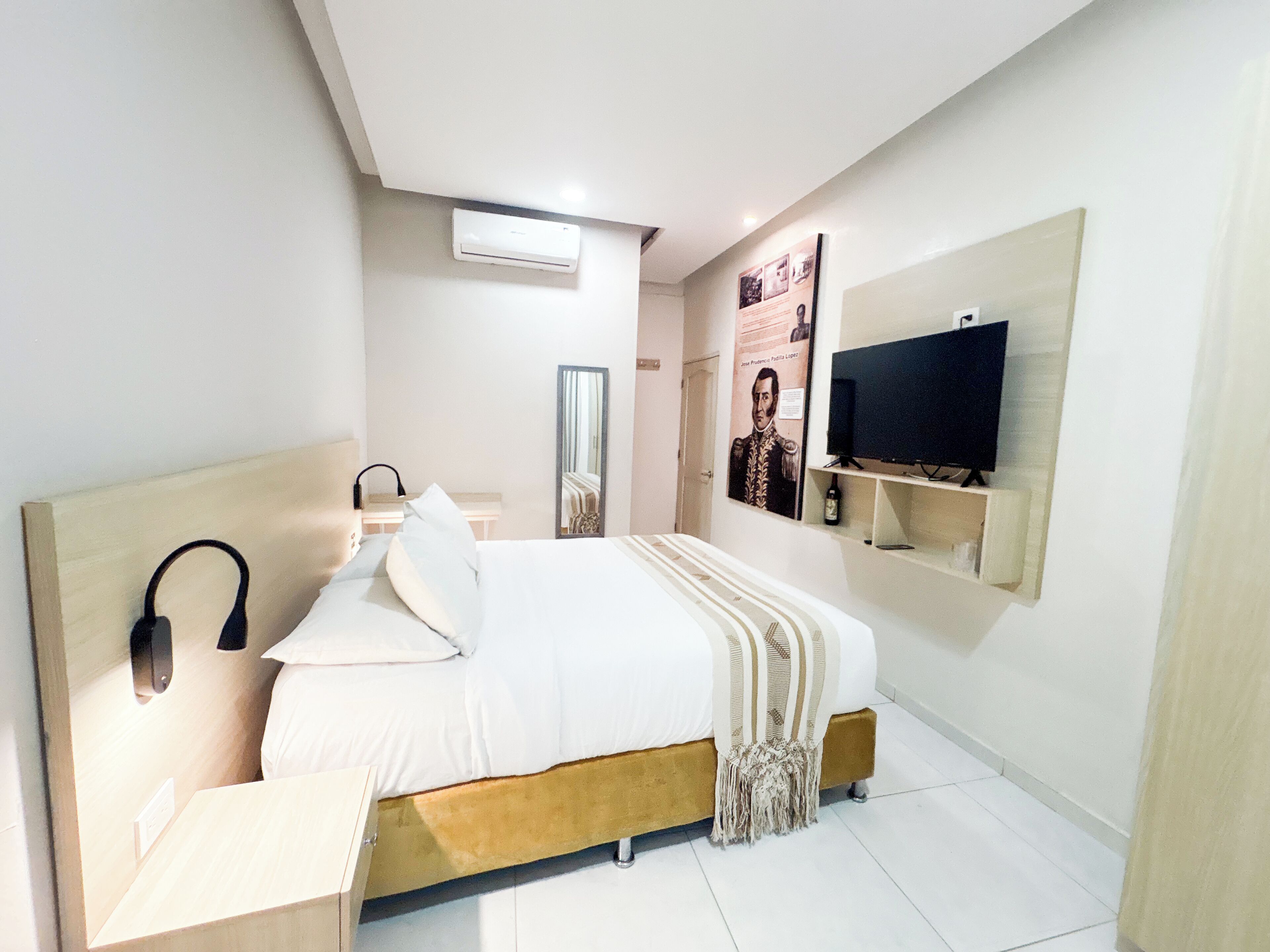 Ein modernes Schlafzimmer mit Bett, Nachttisch, Spiegel, an der Wand montiertem Fernseher und einem Poster.