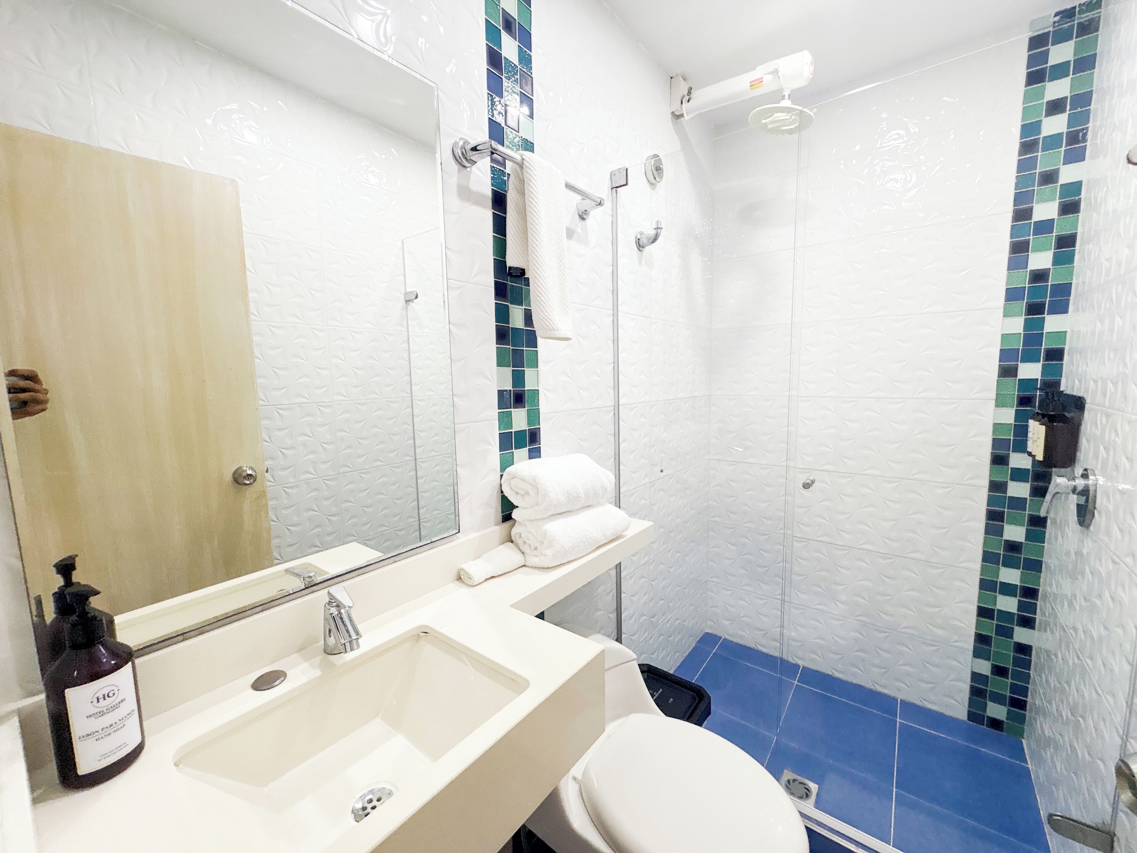Un baño con lavamanos, espejo, toallero y ducha.