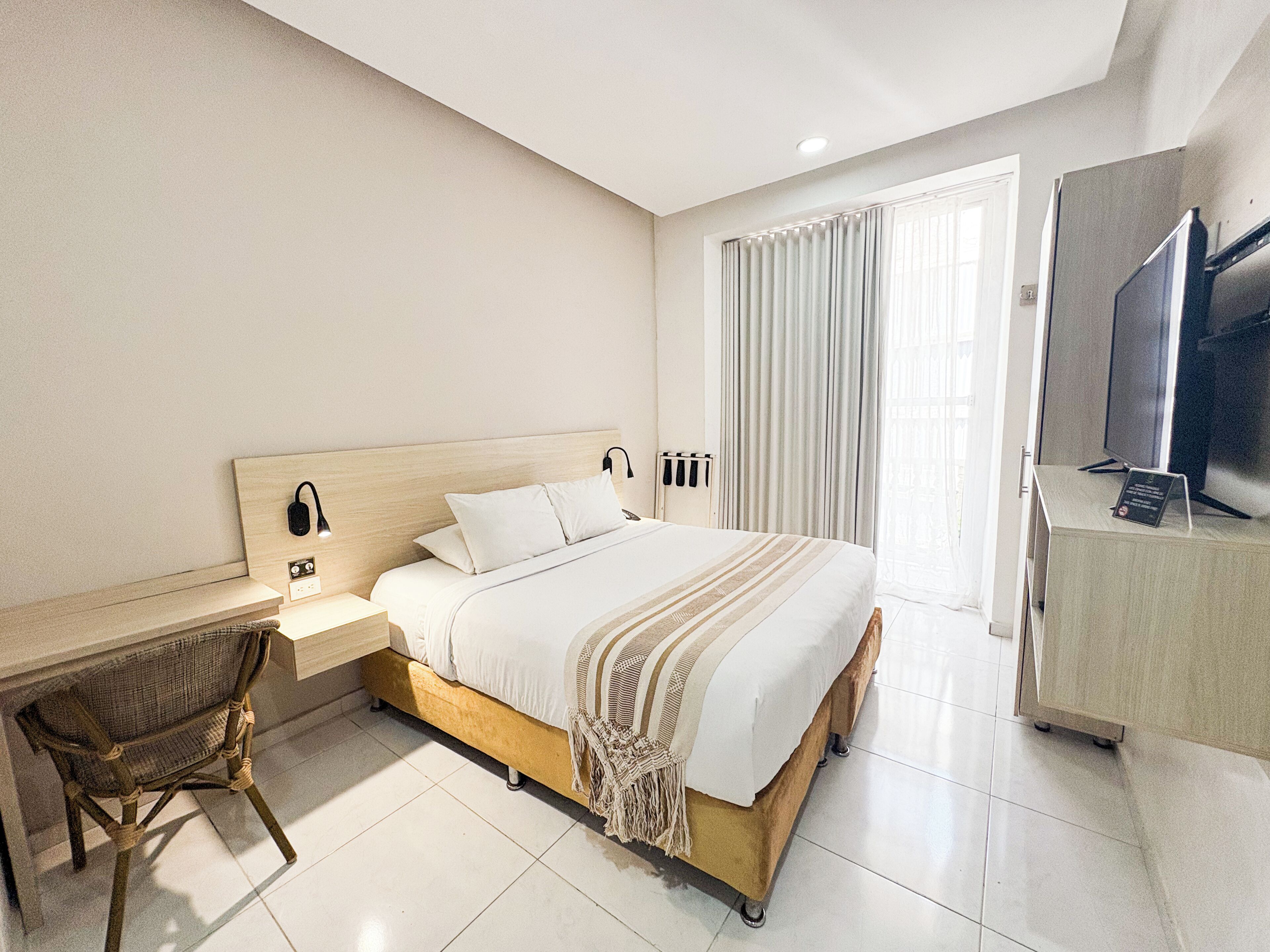 A hotel room with a bed, a desk, a chair, a television, and a large window with curtains.