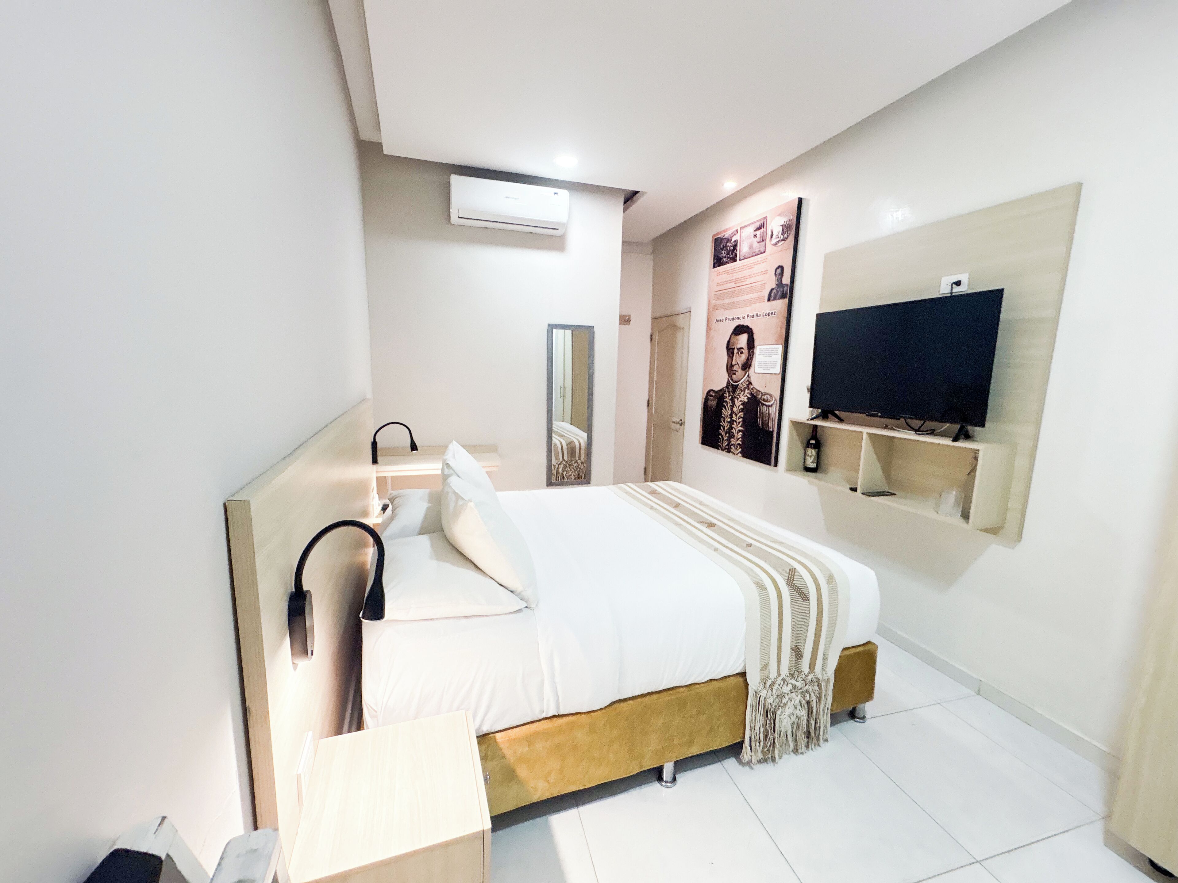 Una habitación de hotel moderna con cama, mesita de noche, espejo, televisor montado en la pared y un cartel en la pared.