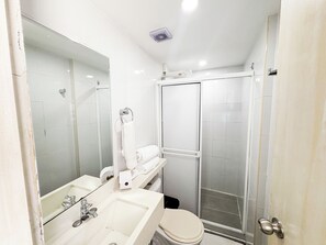 Un baño con lavamanos, espejo, inodoro y ducha con mampara de vidrio.