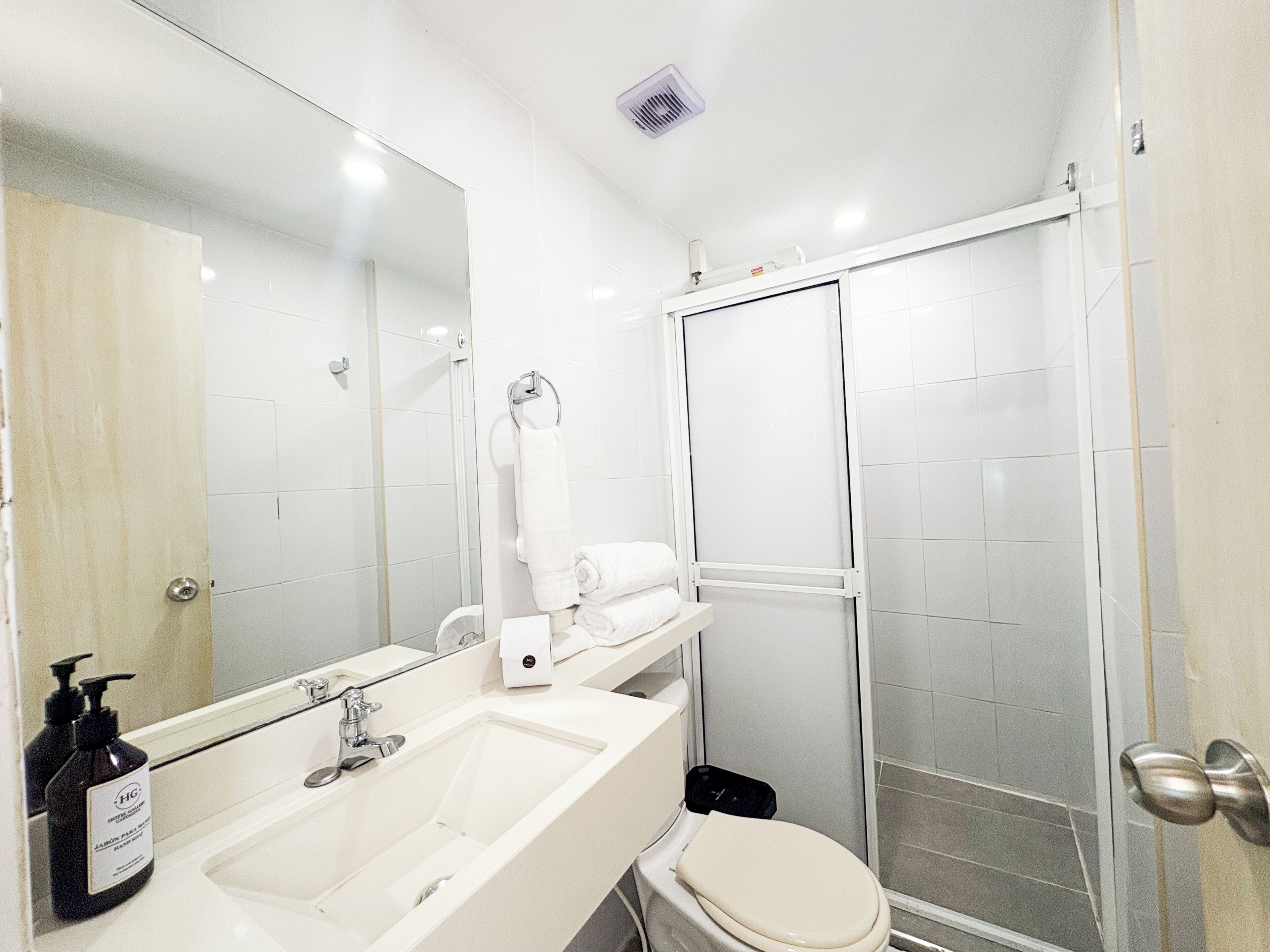 A bathroom with a sink, mirror, towel rack, toilet, and a glass shower enclosure.