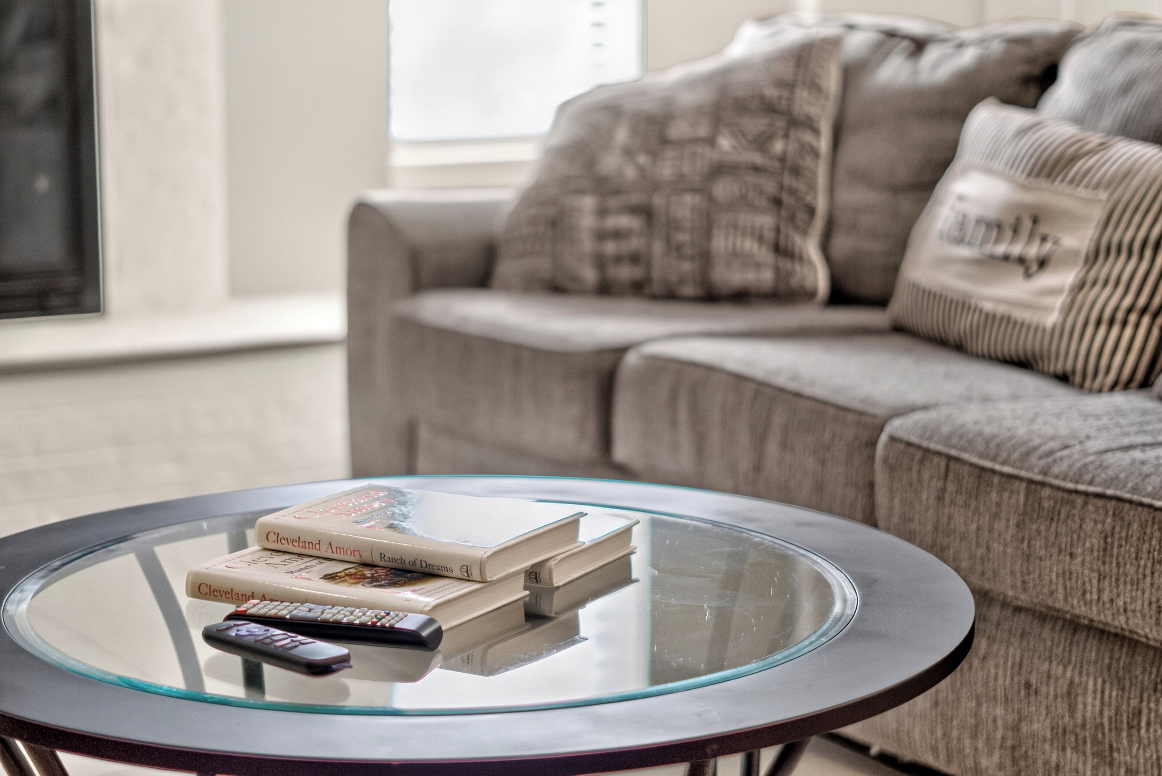 A round glass coffee table with books and a remote control.