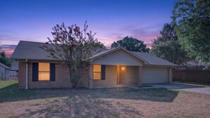 A single-story house with a garage, a small front yard, and a tree with pink flowers. - Peaceful 3 bedroom home in Tyler (Tyler)